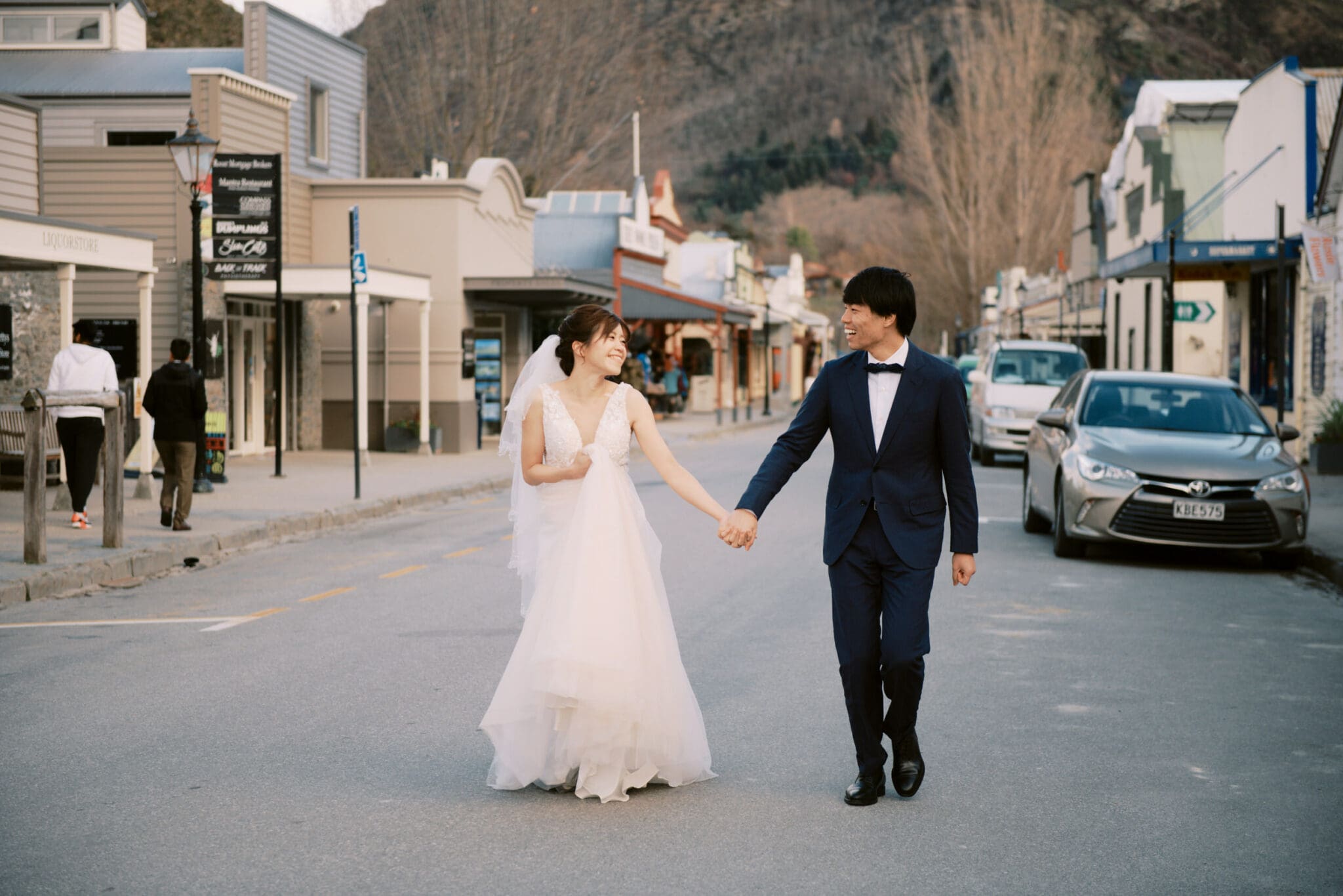 Queenstown Tekapo New Zealand Heli Wedding Elopement Pre-Wedding Shoot Photographer クイーンズタウン　テカポ　ニュージーランド　エロープメント 前撮り　フォトウェディング　結婚式 | Bride and groom holding hands while walking down a street in Tekapo during their pre-wedding shoot.